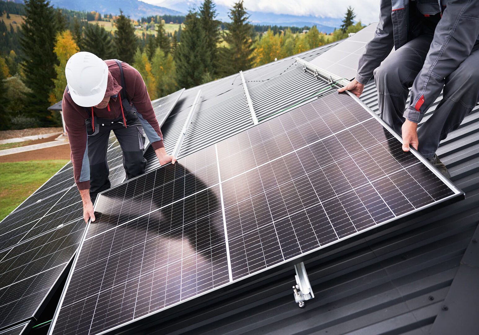 Builders building photovoltaic solar module station on roof of house. Men electricians in helmets installing solar panel system outdoors. Concept of alternative and renewable energy.